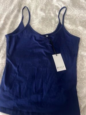 Mörkblå linnetopp från RYVLS - Snygg mörkblå linnetopp från RYVLS med tunna axelband och enkel, stilren design. Perfekt att matcha med jeans eller kjol för en avslappnad look. Tillverkad i mjuk bomull som känns skön mot huden.