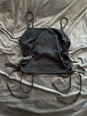 Bikbok Svart croppad linnetopp med snörning - Trendig svart linnetopp med tunna axelband och snörning i sidorna som ger en justerbar, croppad look. Perfekt att styla med jeans eller kjol för en cool och enkel outfit.