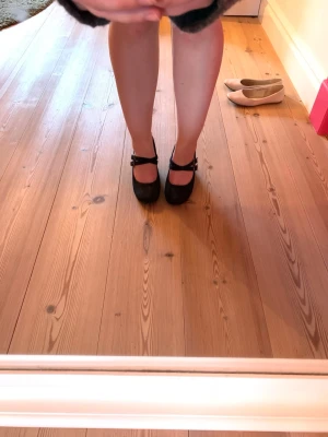 Svarta Mary Jane-pumps med remmar - Snygga svarta Mary Jane-pumps med dubbla remmar och spännen. Skorna har rund tå och klack i mellan-höjd. Materialet är mockaimitation som ger en mjuk och stilren look. Perfekta för dig som vill ha en klassisk men trendig stil.