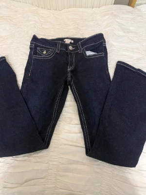 Mörkblå bootcut jeans med kontrastsömmar - Snygga mörkblå bootcut jeans med vita kontrastsömmar och dekorativa fickor både fram och bak. Jeansen har klassisk femficksdesign och silverfärgade knappar. Perfekta för en avslappnad och trendig look.