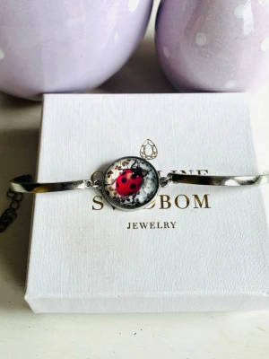 Armband i rostfritt stål  - Armband i rostfritt stål med berlock och nyckelpiga, okänt märke. Justerbart och nytt!