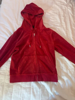 Rött Juicy Couture set  - Säljer en röd hoodie från Juicy Couture i mjuk velour. Hoodien har dragkedja framtill, två stora fickor och justerbar huva med snören. Perfekt för dig som gillar retrostil och vill ha något riktigt bekvämt. Tröjan är i storlek M och byxorna är storlek S men funkar som M också. Pris kan diskuteras! ❤️