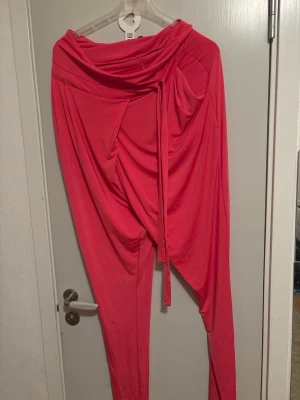 Rosa draperade leggings med knytband - Unika rosa leggings med draperad design och knytband i midjan. Modellen har en lösare passform upptill och smalnar av vid benen. Tillverkade i ett mjukt och stretchigt material som ger en cool och trendig look.