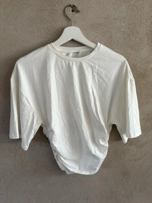 Vit croppad t-shirt med snörning - Säljer en vit croppad t-shirt med snörning i sidan. T-shirten har rund halsringning och korta ärmar. Tillverkad i mjuk bomull och har en clean, enkel look som passar till det mesta.