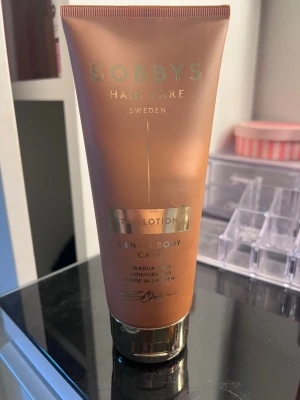 Bobbys Tan Lotion Brun-utan-sol - Brun-utan-sol lotion från Bobbys Hair Care Sweden. Tuben är kopparfärgad med gulddetaljer och innehåller en gradvis brun-utan-sol-kräm som återfuktar huden. Perfekt för dig som vill ha en naturlig solkysst look året runt.