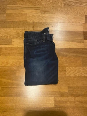 Mörkblå slim fit jeans från hunkydory  - Säljer ett par mörkblå slim fit jeans från hunkydory med klassisk femficksdesign och snygga slitningar framtill. Jeansen har normal midja och smal passform hela vägen ner. Perfekta till sneakers och t-shirt för en avslappnad look. Ham på bilden är 175 och jeansen är lite långa och lite för stora i midjan