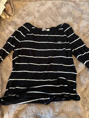Svartvit randig långärmad topp - Svart långärmad topp med vita horisontella ränder och en bröstficka. Avslappnad passform och mjukt material, perfekt för en chill look. Passar till jeans eller kjol för en enkel stil.