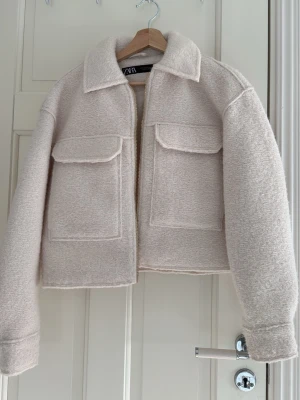 Beige teddy liknade jacka ifrån Zara - Säljer en vit Teddy liknade jacka från Zara med två stora bröstfickor och dragkedja framtill. Jackan har en boxy passform, klassisk krage och är gjord i ett mjukt, ull-liknande material. Perfekt nu på våren, och ger en clean trendig look. Jackan är aldrig använd och i helt nytt skick. Kan även sänka priset lite grann!