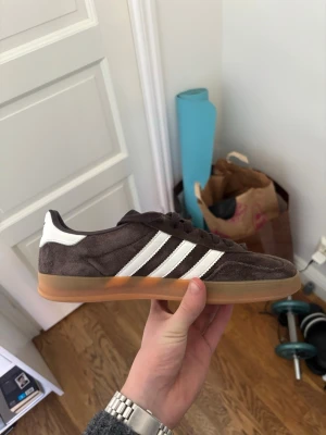 Bruna Adidas Gazelle 42 2/3 - Jättesnygga Adidas Gazelle i storlek 42 2/3. De är i toppskick och jag har knappt använt dem. Har sprayat på impregneringsspray så de tål regn osv. Säljer för att jag ska köpa en storlek större.