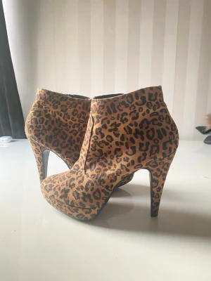 Leopardmönstrade stövletter med klack - Säljer ett par snygga stövletter med leopardmönster och hög klack. Skorna har rundad tå och dragkedja på insidan. Materialet ser ut att vara mockaimitation i bruna och svarta toner. Perfekta för dig som vill sticka ut med din stil.