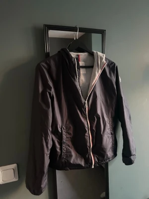 Moncler windbraker 14y - Jackan är barn model storlek 14 y passar på folk upp till 166Snygg svart vindjacka från Moncler med dragkedja framtill och huva. Jackan har grått innerfoder och två fickor med knappstängning. Perfekt för dig som vill ha en stilren och lätt jacka till vardags. Klassisk Moncler-logga på ärmen. Jackan är 