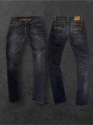 Selvage Nudie Jeans - Säljer ett par mörkblå jeans från Nudie Jeans med klassisk femficksmodell och kontrastsömmar. Jeansen har smal passform och är tillverkade i denim med snygga slitningar och detaljerade bakfickor med Nudie-logga. Selvage som slits med tiden!