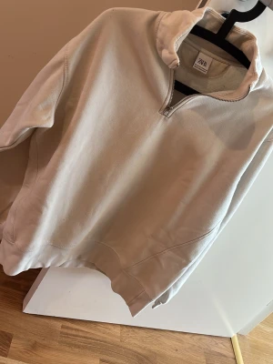 Beige halfzip hoodie från Zara - Hej! Säljer en stilren half zip-tröja från Jack & Jones i storlek M. Tröjan är i en ljus, neutral färg som passar till det mesta och har en modern, avslappnad passform med hög krage och kort dragkedja. Den är i fint skick och sparsamt använd. Säljes då den tyvärr blivit för liten för min son. Perfekt som vardagströja eller för lager-på-lager under kyligare dagar.