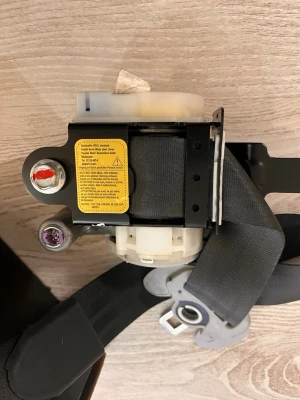 Bilbälte med rullmekanism svart - Säljer ett svart bilbälte med rullmekanism och metallfästen. Bältet har en tydlig varningsetikett i gult och är tillverkat i slitstarkt tyg och metall. Perfekt som reservdel till bilen eller för dig som behöver byta ut ett trasigt bälte.