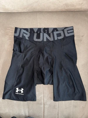 Svarta kompressionstights Under Armour - Säljer ett par svarta kompressionstights från Under Armour med bred resår i midjan och logga på benet. Tightsen har ficka på sidan och är tillverkade i ett stretchigt funktionsmaterial (HeatGear) som andas. Perfekta för träning eller löpning.