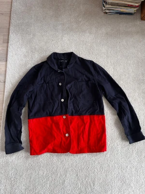 Svart och röd overshirt med fickor - Snygg overshirt i svart och rött med två stora bröstfickor och knäppning framtill. Overshirten har en avslappnad krage och raka ärmar. Skön canvas
