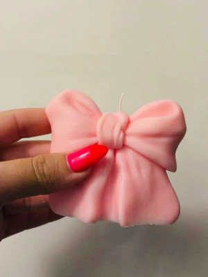 Rosa rosettformad dekorationsljus - Säljer ett ljus i form av en rosett i ljusrosa färg. Ljusets design är söt och dekorativ, perfekt som prydnad eller present. Kommer i en matchande rosa förpackning med genomskinligt fönster. Tillverkat av vax.