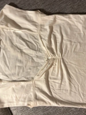 Vit axelbandslös tubtopp - Säljer en stilren vit axelbandslös tubtopp med rynkad detalj framtill. Toppen har en enkel och clean look som passar perfekt till många olika outfits. Materialet känns mjukt och följsamt.