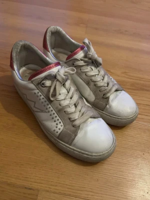 Zadig & voltiare skor - Snygga sneakers i vitt och grått med rosa detalj på hälen. Skorna har en cool blixtdesign på sidan och små silverfärgade nitar. Ovandelen är i läder och mocka, med klassisk snörning och låg profil. Perfekta för dig som gillar en sportig och trendig look.