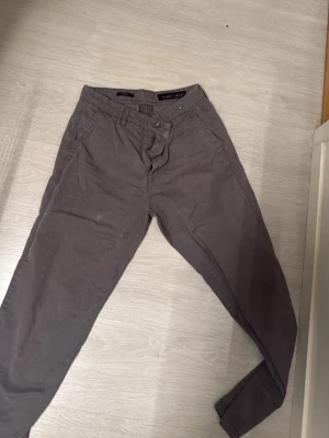 Mörkgrå chinos från Zara Man - Snygga mörkgrå chinos från Zara Man med klassisk rak passform. Byxorna har sidofickor, bälteshällor och två bakfickor med knapp. Tillverkade i mjukt bomullstyg som ger en skön känsla och stilren look.
