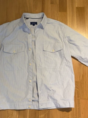 Blårandig skjorta från Eton - Säljer en snygg blårandig skjorta från Eton med klassisk krage och två bröstfickor med knappar. Skjortan har långa ärmar och vita knappar framtill. Perfekt för dig som gillar stilrena detaljer och tidlös design. Ny pris ca 4000kr, använd fåtal gånger. Pris kan diskuteras.