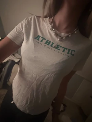 Vit t-shirt med text - Säljer en vit t-shirt med grön text 'ATHLETIC WEST COAST CHALLENGE' på bröstet. Från UNIQLO young