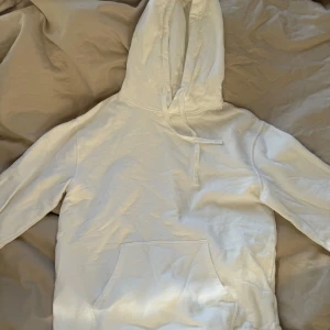 Vit hoodie med magficka - Säljer en enkel och stilren vit hoodie med stor magficka och huva. Hoodien har långa ärmar och ribbade muddar vid ärmslut och nederkant. 