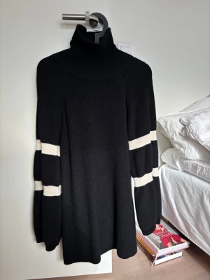 Svart poloklänning med vita ränder - Stickad svart poloklänning från ARKET med breda vita ränder på ärmarna. Tröjan har en hög polokrage och långa, lite vidare ärmar. Perfekt för dig som gillar en stilren och trendig look. Storlek XS och mycket bra skick!! Passar även som S🫶🫶