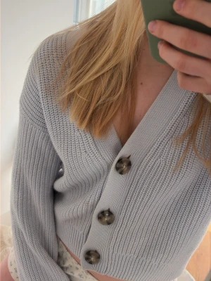 Ljusblå kofta med stora knappar - Trendig ljusblå kofta med tre stora, mönstrade knappar framtill. Den passar skitsnyggt med ett linne. Har inte använts mycket alls, den säljs inte längre. Det finns en liten fläck bredvid en knapp som syns på bilden, däremot så ser man den knappast.