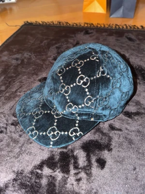 Säljer en äkta Gucci GG Velvet baseballkeps i mycket fint skick. - • Original från Gucci • Klassisk GG-monogram design • Lyxigt sammetstyg i mörk blå/grön ton • Röd/rosa insida med Gucci-märkning • Tillverkad i Italien • Mycket sällsynt keps Kepsen är sparsamt använd och i väldigt bra skick utan större slitage. En riktigt snygg statement-accessoar som passar både vardag och mer uppklädda outfits.  Storlek: (fyll i storlek om du vet, t.ex. S/M eller cm)  Nypris: ca 5000-6000kr  Säljes för: 4000kr  Kan skickas eller mötas upp. Hör av dig vid frågor!