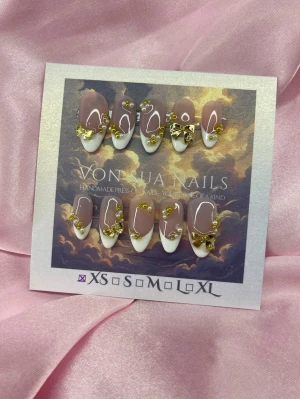 PearlMuse (XS);Medium Almond - Snygga handgjorda press-on naglar i en medium almondform. Naglarna har en nude bas med vit fransk tipp och dekoreras med guldfärgade 3D-rosetter och pärlor. Perfekt för dig som vill ha en lyxig och unik nagelstil. Handgjorda och riktigt trendiga!XS: 14 mm, 11 mm, 11,5 mm, 10 mm, 8 mm 