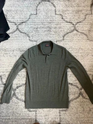 Olivgrön merinoullströja från Morris - Snygg olivgrön långärmad tröja från Morris i mjuk merinoull. Tröjan har klassisk pikékrage och två knappar framtill. Perfekt för dig som gillar stilrena och tidlösa plagg med en modern touch.