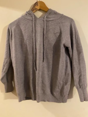 Grå hoodie med dragsko - En enkel och stilren grå hoodie med huva och dragsko. Tillverkad i mjukt stickat material som känns skönt mot huden. Långa ärmar och ribbade muddar vid ärmslut och nederkant. Perfekt för en avslappnad look. Hoodien har en tajt passform