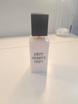 Katy Perry's Indi parfym 10m ingen förpackning då den tog upp mycket plats menl aldrig använd  - Katy Perry's Indi parfym i en stilren, vit rektangulär flaska med svart fyrkantigt lock och gulddetaljer. Flaskan har enkel svart text på framsidan och ger ett modernt intryck. Perfekt för dig som gillar unika dofter och snygg design på parfymhyllan. Har dock slängt förpackningen