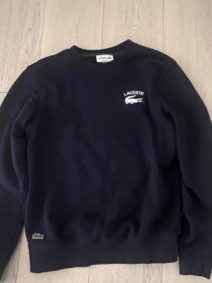 Hoodie Lacoste - Säljer nu denna mörkblå Lacoste hoodie då den blivit för liten för mig. Den är andvänd väl och inga defekter på den. Storlek S. OBS! Priset är ej hugget i sten. 