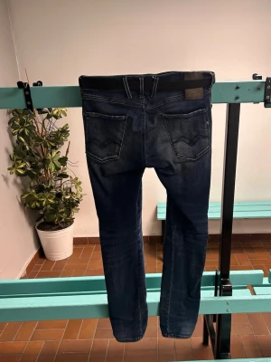 Mörkblå slim jeans från Replay - Snygga mörkblå slim fit jeans från Replay, modell Anbass. Jeansen har klassiska bakfickor med detaljerade sömmar och bälteshällor. Tillverkade i stretchigt denim för extra komfort och en schysst passform. Perfekta för dig som gillar en modern och stilren look.