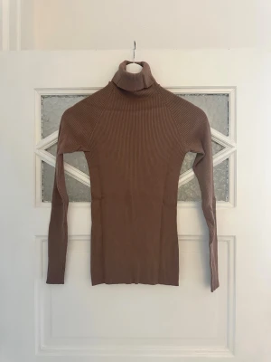 Brun ribbad polotröja - Slimmad brun ribbad polotröja med långa ärmar och hög krage. Knappt använd.