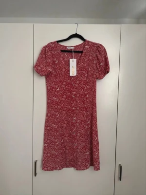 Röd blommig klänning från ONLY - Söt röd kortklänning från ONLY med vitt blommönster. Klänningen har korta puffärmar och v-ringning. Tillverkad i ett lätt och luftigt material, perfekt för varma dagar. Enkel och feminin design som ger en avslappnad men ändå stilsäker look. Pris kan diskuteras (nypris: 330kr)