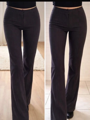 Grå/Svarta kostymbyxor med vita ränder - Snygga grå/svarta kostymbyxor med tunna vita kritstrecksränder och utsvängda ben. Byxorna har hög midja och klassisk passform som ger en stilren siluett. Perfekta för dig som gillar en trendig och tidlös look.