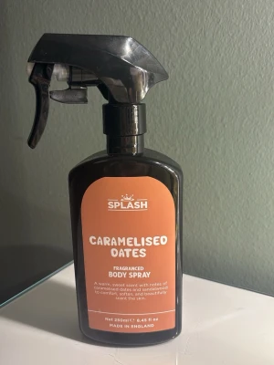 Splash Caramelised Oats Body Spray - Splash Caramelised Oats Fragranced Body Spray i en svart plastflaska med spraymunstycke. Doften har varma, söta toner av karamelliserad havre och sandelträ. Flaskan rymmer 250 ml och har en modern, stilren design med orange etikett.