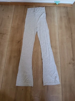 Ljusgrå utsvängda leggings - Säljer ett par ljusgrå leggings med utsvängda ben och hög midja. Tillverkade i ett mjukt och stretchigt material som sitter skönt på kroppen. Perfekta för en avslappnad och trendig look.