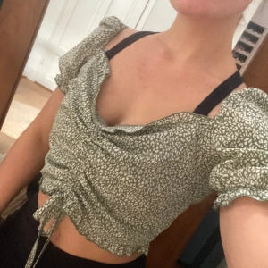 Topp / blus  - Söt liten blus i grön vita fläckmönster.  Har diskret dragkedja på sidan. Med snören i mitten kan man själv ändra hur liten/ stor yta den skall täcka framtill.