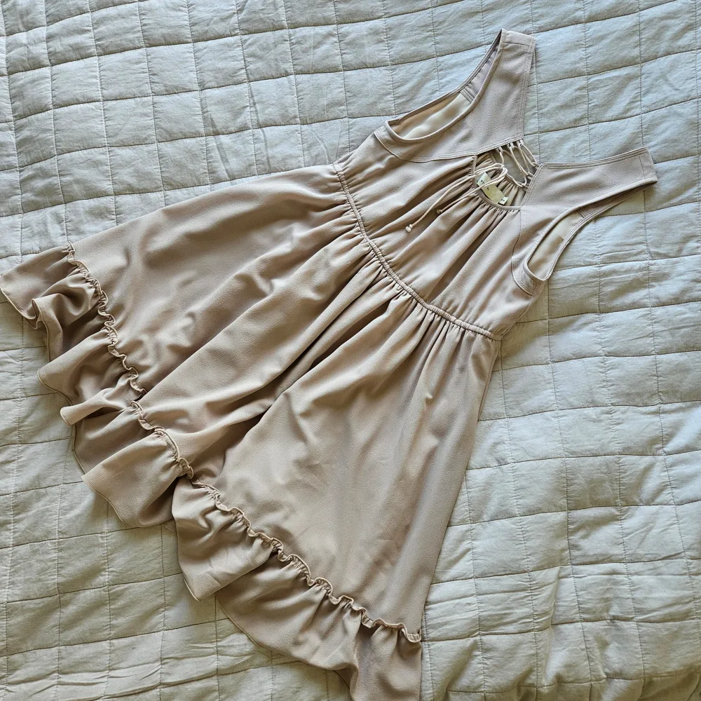 Kort, klockad modell med volang och knytning. Beige. Längd 85 cm. Storlek S/M. Mekot.
