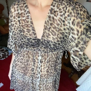Klänning i leopardmönster - Så fin klänning med leopardmönster. Ganska transparent så perfekt till stranden eller med en klänning under. Kan justeras i midjan. Sitter snyggt och är bekväm, bra skick! Slutar på mitten av låret ungefär