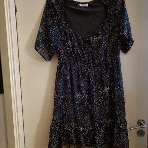 Blommig klänning  - Aldrig använd. Ärmarna är genomskinliga, resår under bysten. Axelbredd ca 40cm, längd ca 90cm