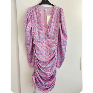 Adoore kläning  - En helt ny klänning från adoore med puffärmar och ett vackert blommönster. Klänningen har en v-ringning och en figursydd passform. Den är perfekt för en festlig tillställning eller en kväll ute. Prislappen är kvar. Priset kan diskuteras:)