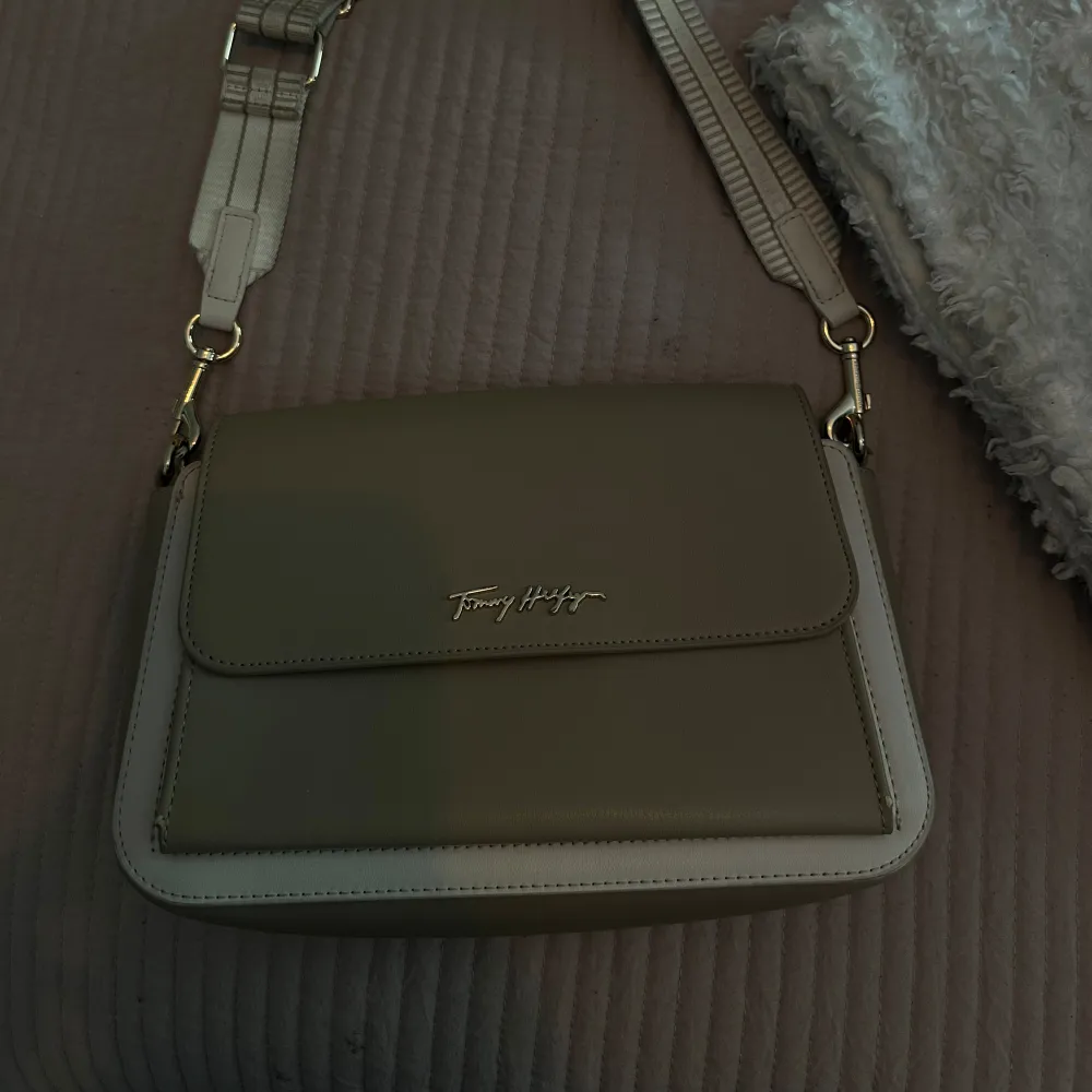 Liten axelremsväska som även går att ha som clutch från Tommy Hilfiger.  Beige med guldiga detaljer  Köpt för 170euro = cirka 1700kr . Väskor.