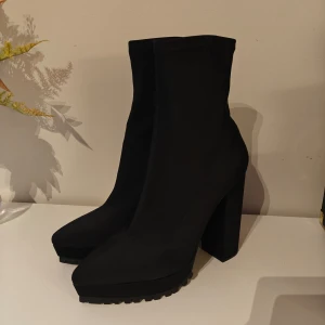 Svarta högklackade boots  - High heel neoprene boots från Nelly Aldrig använda, i toppen skick, bara testade i hemmet därav lite synlighet av användning på sulorna. Överdelen av skorna är "mjukt" och rörligt material. Material: neopren Org. pris 599kr. Säljs ej längre online