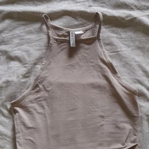 Beige linnetopp från H&M Divided - En enkel och stilren beige linnetopp från H&M Divided. Toppen har smala axelband och en hög halsringning. Köpt för 1 år sedan, storlek S. 