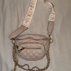 Steve Madden crossbody/axelväska  - Kan användas som axelremsväska, axelväska och runt midjan då bandet är avtagbart och justerbart. Den går att använda som axelremsväska även med kedjan. Ena sidan av tygbandet är förstörd, finns inga andra defekter.
